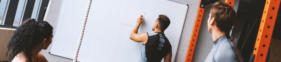 A group of people in a gym discussing at a whiteboard