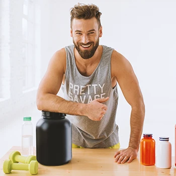 A buff male with a lot of pre-workout and protein powders on a table