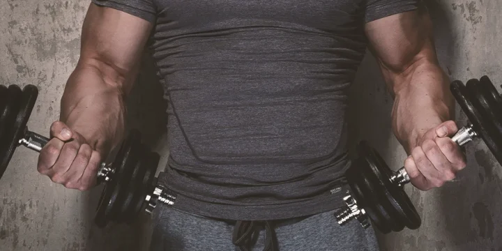 A man in the gym lifting two dumbbells