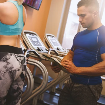 A gym trainer taking notes down on a clipboard while someone is working out