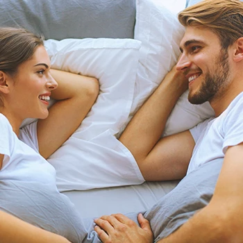 A couple in bed looking at each other smiling