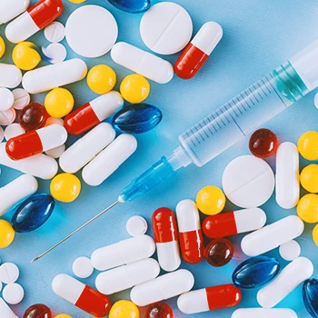 A variety of pills and a syringe on a blue table