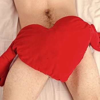 Naked man with a heart shaped pillow on his lower body