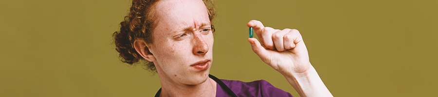 A doctor holding a green pill with confusion