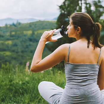 A woman drinking water in the mountains while doing yoga