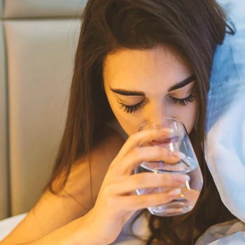 Close up shot of a woman drinking a glass of water while in bed