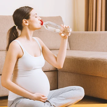 A pregnant woman drinking water indoors while doing yoga