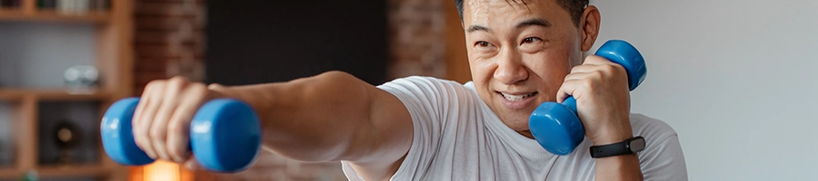 Asian man holding two dumbbell performing exercises indoors