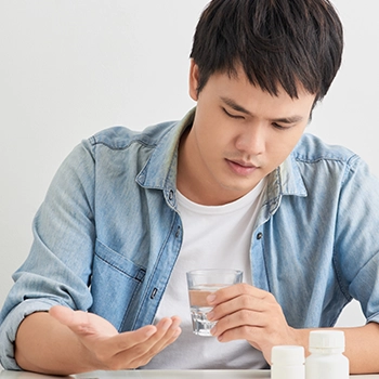 Clueless guy looking at his supplement pill while holding a glass of water