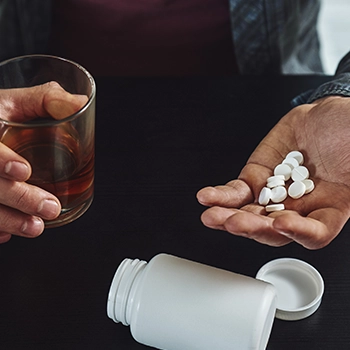 Holding an alcohol and white pills with both hands