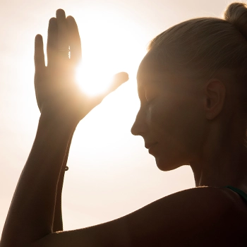 A woman meditating outdoors during a sunset