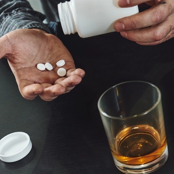 Holding white pills and an alcohol glass on table