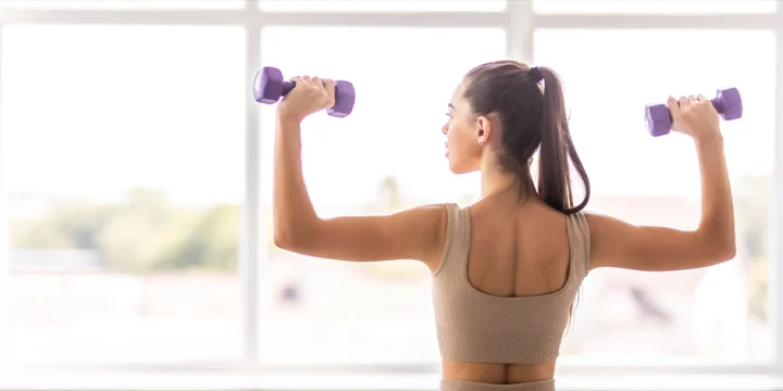 Holding two dumbbells while showing back to the camera