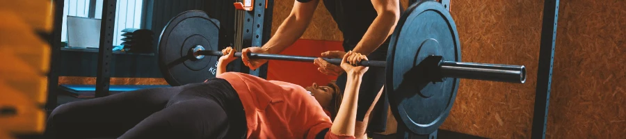 A woman being helped with lifting a barbell in the gym