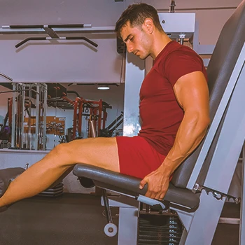 A buff male doing leg extensions on a machine in the gym to target outer quad