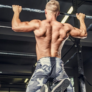 Topless man in military pants doing pull ups