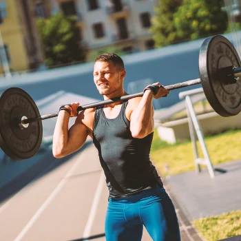 A man is lifting and doing barbell exercises outside