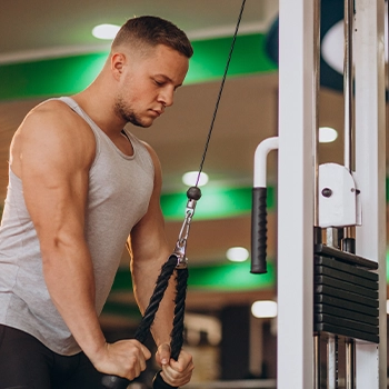 A guy in tank top doing straight arm pulldowns