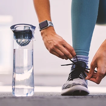 A person in the gym tying a shoe with a bottle of water on the side
