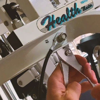 A person in the gym removing an old cable from a machine