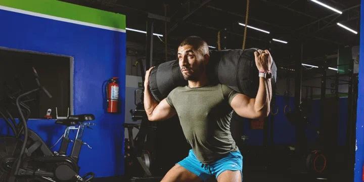 A buff male doing sandbag leg workouts in the gym
