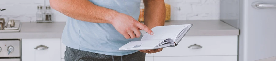 A person in the gym looking at diet plans in a book while in a kitchen