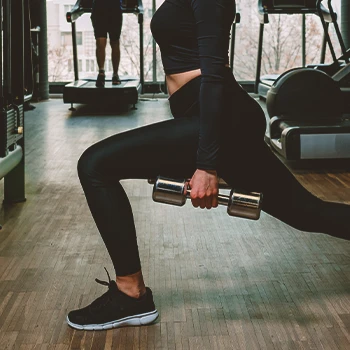 A teenager doing dumbbell lunges in the gym