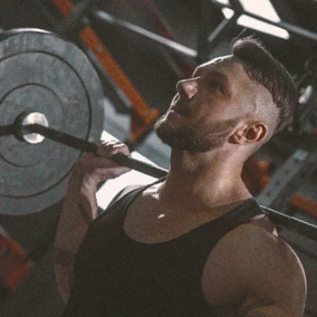 A buff male lifting a barbell in the gym