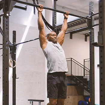 A buff male at the gym doing dead hangs