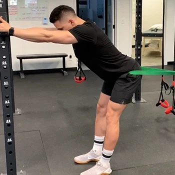 A man doing banded standing hip thrust in the gym