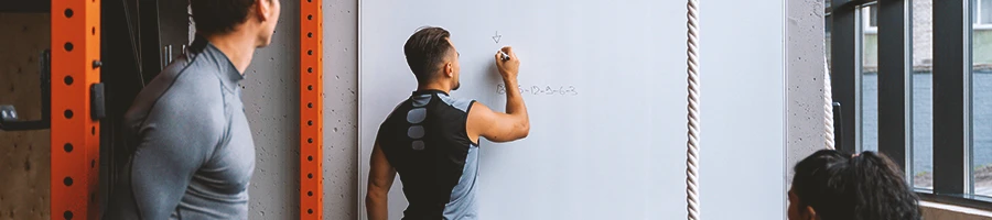 A coach writing down on a whiteboard differences between HIIT and LISS