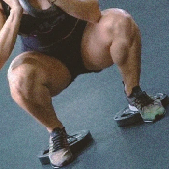 A person doing elevated heel squats on weight plates at the gym
