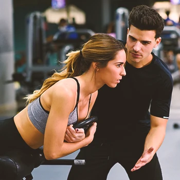 A coach at the gym helping a person with upper-lower workout