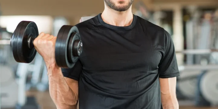 A guy in the gym working out using a dumbbell