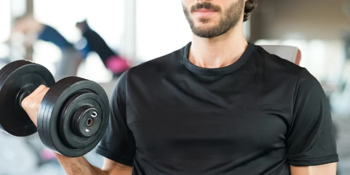 A muscular man working out in the gym with a dumbbell